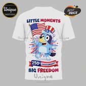 White tee with blue dog cartoon holding US flag; text 'LITTLE MOMENTS,' '250th ANNIVERSARY,' 'BIG FREEDOM' in red, white, blue!