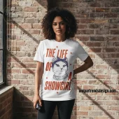 White graphic tee with distressed red text 'THE LIFE OF A SHOWGIRL' featuring a cartoon cat wearing a purple bandana and spiked collar!
