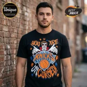 Black t-shirt featuring graphic text You Are New York Knicks Uncursed with a cartoon mascot and basketball design!