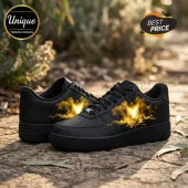 Black sneakers with glowing yellow phoenix fire design on side panels and black laces sitting on stone path!