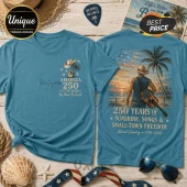 Teal t-shirt featuring front pocket logo and large back print of a cowboy with an American flag guitar on a beach.!
