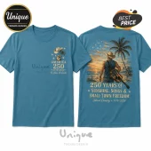 Teal t-shirt with American 250th anniversary graphic featuring a cowboy, acoustic guitar, palm tree, and sunset beach scene.!