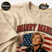 Beige graphic t-shirt featuring Barry Manilow portrait, American flag backdrop, firework motif, and red text overlay.!