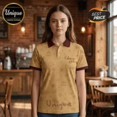 Woman wearing a tan polo shirt with maroon collar and cuffs, featuring a Gilmore Girls logo and coffee and book pattern.!