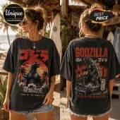 Black vintage-wash t-shirt featuring Godzilla graphic, sunset, palm trees, and Japanese text in red and orange colors.!