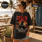 Woman wearing black acid-wash Godzilla graphic t-shirt with red sunset, palm trees, and Japanese text on a sandy beach.!