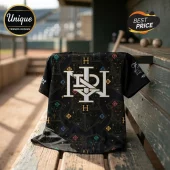 Black baseball jersey featuring gold and white Hogwarts-inspired crest patterns on a wooden bench in a baseball dugout.!