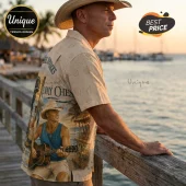 Man wearing a cream-colored Kenny Chesney graphic print button-down shirt with a coastal seashell pattern background.!