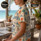 Woman wearing a beige button-down shirt with Mickey Mouse, tropical flowers, palm trees, and ukulele print at a beach.!
