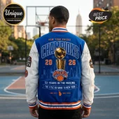 Back view of a blue and white New York Knicks varsity jacket featuring a gold championship trophy graphic and 2026 text.!