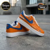 Orange leather New York Knicks sneakers with blue swoosh, white soles, and team branding on an outdoor concrete surface.!