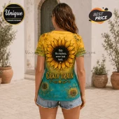 Woman wearing a short-sleeve yellow and teal t-shirt with a sunflower print and the text Ride the madness, never look back.!