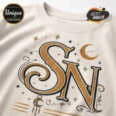 Off-white crewneck sweatshirt featuring gold and black celestial graphic print with letter initials SN, moons, and stars.!