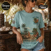 Woman wearing a faded teal t-shirt with Rat Fink Beach Club graphic, palm trees, surfboard, and beach hut design.!