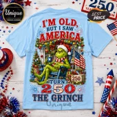Light blue t-shirt with Grinch graphic, American flag, Christmas tree, and text reading I'm old but I saw America turn 250.!