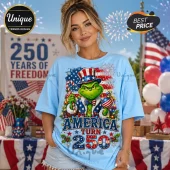 Light blue t-shirt with a Grinch wearing an Uncle Sam hat, American flag background, and America 250th anniversary text.!