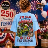 Light blue t-shirt with Grinch graphic, American flag, Christmas decor, and text stating I am old but I saw America turn 250.!