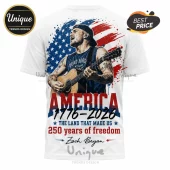 White t-shirt featuring a Zach Bryan illustration, acoustic guitar, American flag background, and 1776-2026 text graphics.!