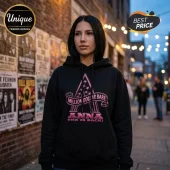 Woman wearing a black hoodie with pink Million Dollar Babe Anna graphic and star accents against a brick wall background.!