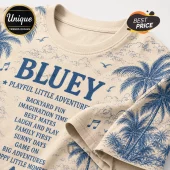 Bluey Playful Adventures Special Edition T-Shirt in beige with blue tropical palm tree prints and motivational text.