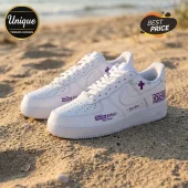 White leather sneakers with purple custom text and cross graphics positioned on a sandy beach.!