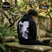 Man wearing a black cotton hoodie with a blurry, abstract light graphic and FKJ text on the back, seated outdoors.!
