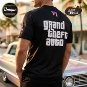 Black t-shirt featuring Grand Theft Auto logo text, a gradient Roman numeral VI, and sleeve graphic on a person outdoors.!