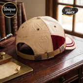 Beige faux leather baseball cap with debossed diamond, 1911 text, and red velvet side panels on a wooden desk.!