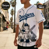 Man wearing a white LA Dodgers baseball jersey with a blue KAWS-style character graphic holding a bat and city skyline.!