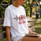 White cotton t-shirt featuring a black heartbeat EKG line graphic and the red KitKat logo with text below.!