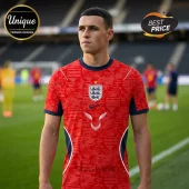 Phil Foden wearing a red England soccer jersey with navy trim, central crest, and repeating ENG pattern on a pitch.!