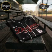Black Los Angeles Dodgers baseball jersey with red script lettering, white piping, and splatter pattern on a wood bench.!