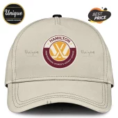 PWHL Hamilton Est 2026 off-white cap with a circular logo featuring crossed hockey sticks and maroon and gold branding.