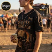 Man wearing black Queens of the Stone Age baseball jersey with gold skull, cactus, and bone graphics at a desert festival.!